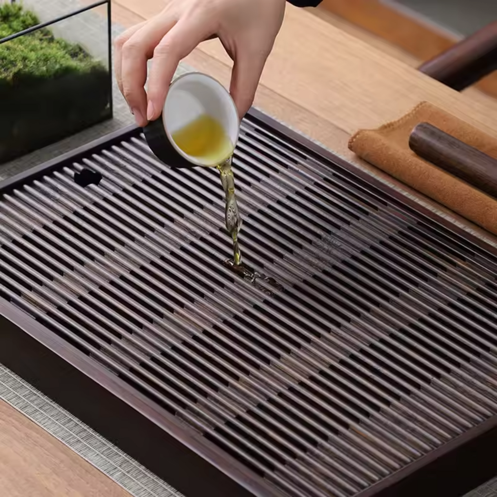 Hand pouring tea over large bamboo tea tray with slatted surface and drainage