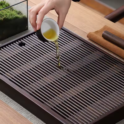 Hand pouring tea over large bamboo tea tray with slatted surface and drainage